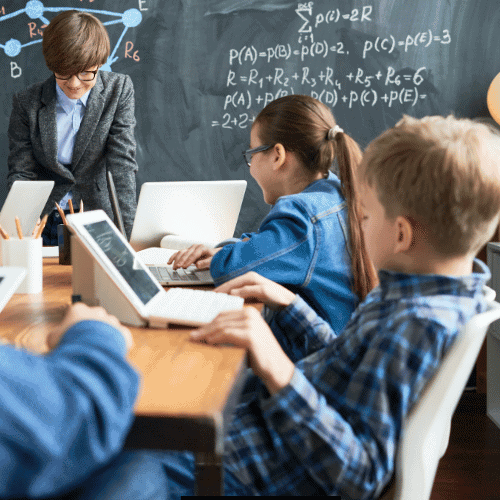 Kinder an einem Tisch vor einer Kreidetafel die sich etwas erklären.